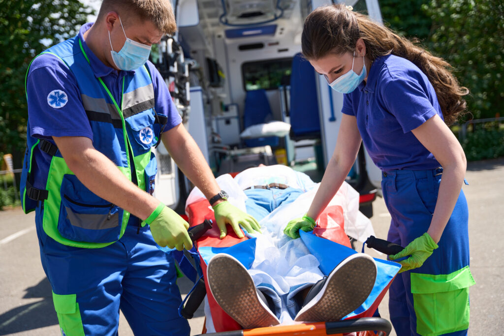 Two paramedics transport a patient on a stretcher towards an ambulance.